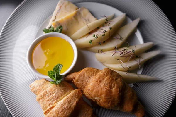 Morgenmad. Croissanter, pære, honning, ost, på en hvid tallerken - Stock-foto