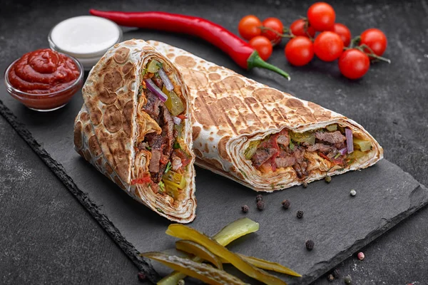 Shawarma soslu, soğanlı, turşulu, otlu ve acı kırmızı biberli, siyah beton arka planda.