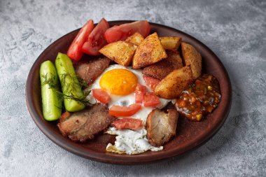 Ev yapımı kahvaltı, salatalık, kızarmış patates, sahanda yumurta, domuz pastırması, domates ve ev yapımı sos.