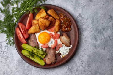 Ev yapımı kahvaltı, salatalık, kızarmış patates, sahanda yumurta, domuz pastırması, domates ve ev yapımı sos.