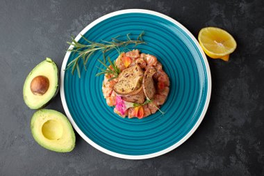 Avokadolu somon tartare, mavi çizgili tabakta, kireç ve kızarmış ekmekle, koyu bir arka planda.