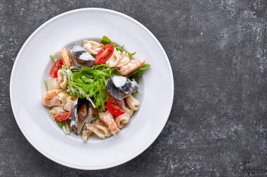 Kabuklu deniz ürünleri salatası, mürekkep balığı, karides, yuvarlak beyaz bir tabakta, gri bir arka planda.