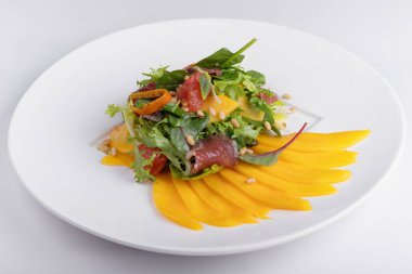 Karışık mango salatası, kurutulmuş et, greyfurt, çam fıstığı ve nane, beyaz bir tabakta, beyaz arka plan