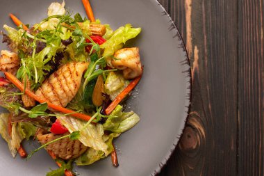 Izgara kalamar, mısır, havuç, domates ve marullu deniz ürünleri salatası.