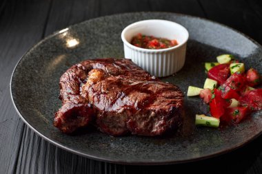 Siyah bir arka planda, siyah bir tabakta sebzeli ve soslu et.