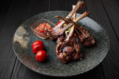 Siyah bir arka planda domates ve sosla siyah bir tabakta kuzu eti.