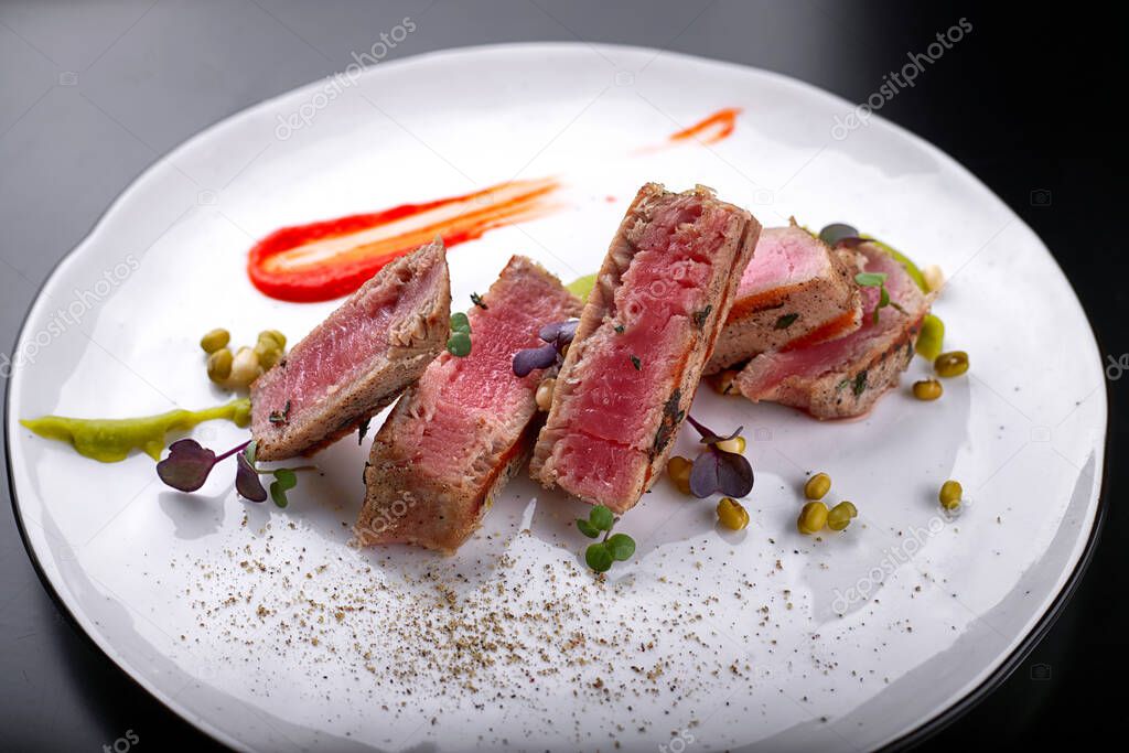 Filet mignon with capers, on a white plate, on a dark background