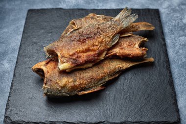 Kızarmış balık sazan balığı, siyah bir taşın üzerinde, gri bir arka planda.