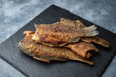 Kızarmış balık sazan balığı, siyah bir taşın üzerinde, gri bir arka planda.