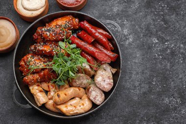 Bira, sosis, kaburga, ızgara kanat ve siyah arka planda üç soslu et.