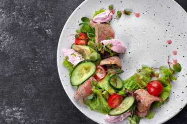 Buzağı ve krem peynirli sıcak salata, beyaz tabakta ve koyu arka planda.