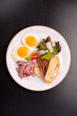 Domatesli sahanda yumurta, jambonlu ciabatta tostu, koyu arkaplanda. Kahvaltı.