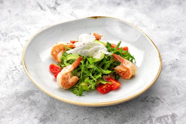 Karides, domates ve roka salatası, beyaz bir tabakta, arka planda.