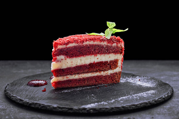 Red velvet cake slice on black stone surface with studio lighting, elegant gourmet dessert concept