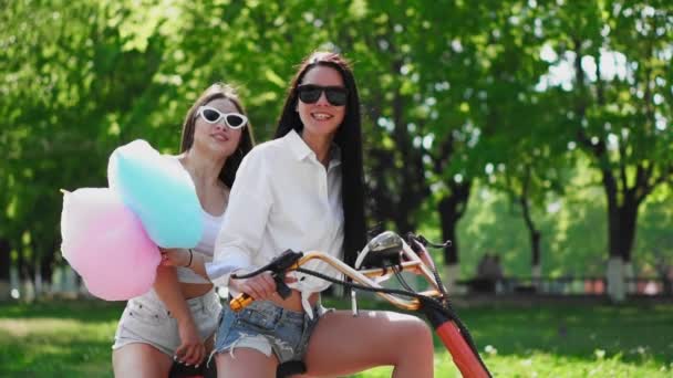 Meninas sexy com algodão doce em shorts curtos montar uma scooter elétrica no parque — Vídeo de Stock