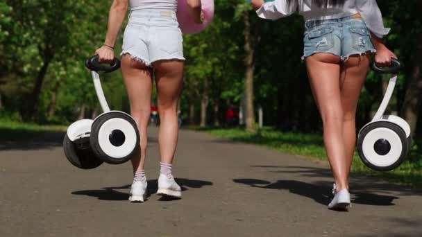 İki genç seksi esmer bağsız kıl ile kısa denim şort ve beyaz t-shirt gri beyaz Segway ve tatlı Pamuk yün taşıyan parkın içinden gitmek — Stok video
