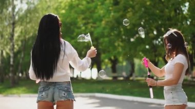 İki güzel genç kızlar seksi kıyafetler içinde gülüyor ve ağır çekimde sabun köpüğü ile oynarken hafta sonu bir Segway parkta sürme sırasında dans