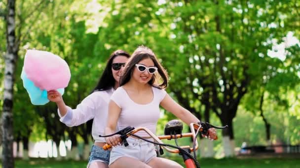 Meninas sexy com algodão doce em shorts curtos montar uma scooter elétrica no parque — Vídeo de Stock