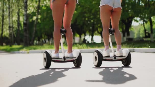 Belles filles brunes minces dans les lunettes de soleil hauts blancs et les cheveux courts ont du plaisir et rire en dansant sur blanc Segways dans le parc — Video