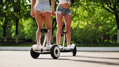 İki güzel genç kızlar seksi kıyafetler içinde gülüyor ve parkta Segway üzerinde hafta sonu sürme sırasında dans