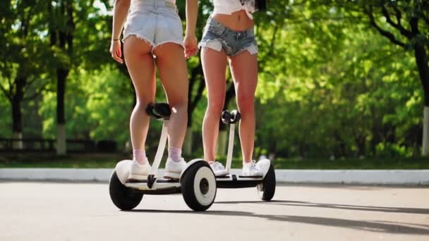 Twee mooie jonge meisjes in sexy kleding zijn lachen en dansen tijdens het rijden op de Segway in het Park in het weekend — Stockvideo