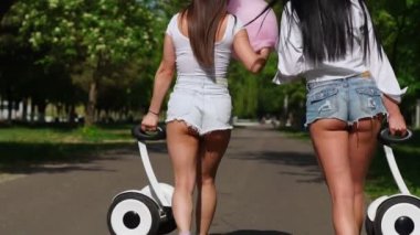 İki kadın kot şort ve beyaz t-shirt yakın - yukarı git arka kamera görüntülemek ve kendi kendine karşı bir scooter elinde taşımak