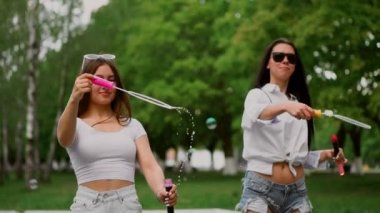 İki güzel genç kız parkta bir Segway kabarcıklar ağır çekimde üfleme parkta sürme sırasında gülüyorsun