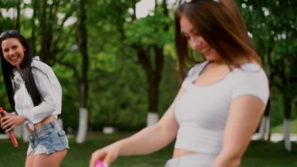 Zwei schöne junge Mädchen im Park lachen, während sie auf einem Segway im Park fahren und Blasen in Zeitlupe pusten — Stockvideo