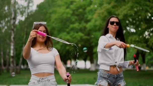 Dos hermosas chicas jóvenes en el Parque se ríen mientras montan un Segway en el Parque, soplando burbujas en cámara lenta — Vídeo de stock