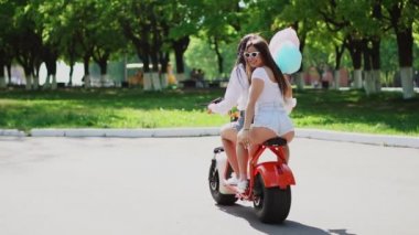 İki güzel kız kot şort parkta bir elektrikli motorla yaz aylarında binmek