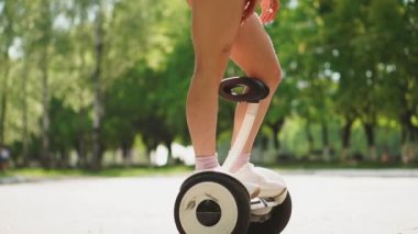 Kız Kısa denim şort ve beyaz t-shirt ağır çekimde Gyroscooter üzerinde sürme güneşli bir günde eğleniyor.