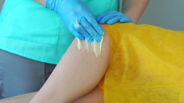 La fille parle au téléphone et sourit lors de l'épilation des jambes dans le salon de beauté. Épilation sur les jambes avec du sucre. clouse-up — Video