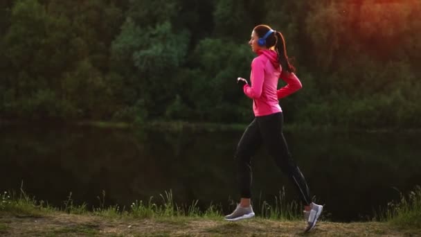 Ein morgendliches Joggen im Park in der Nähe des Teiches in den sonnigen Sonnenstrahlen der Morgendämmerung, bereitet sich das Mädchen auf Mariano und führen einen gesunden Lebensstil — Stockvideo