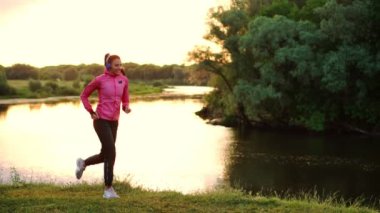 Kulaklığımda uzun saçlı esmer parkta Nehri boyunca gündoğumu pembe bir ceket ve siyah pantolon yaz sabahı çalışır