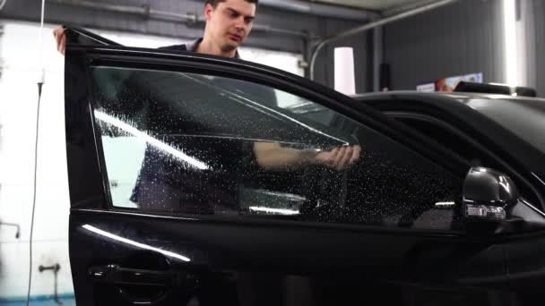 Мастер устанавливает тонированную пленку для автомобильного стекла с феном и лопаткой с бликами света. Тонировка концепции — стоковое видео