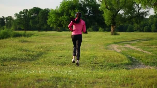 La ragazza corre al tramonto nel Parco lungo lo stagno e ascolta musica in cuffia — Video Stock