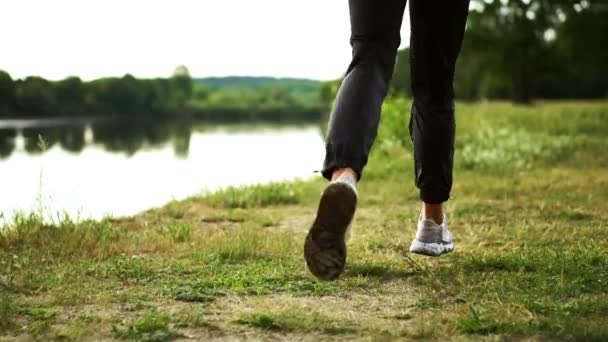 Close-up van voeten op het gras in sneakers langs de rivier loopt — Stockvideo