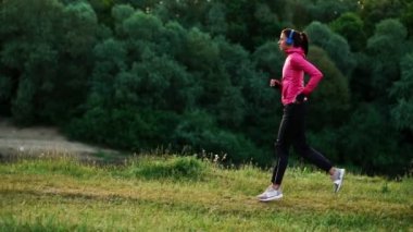 Kulaklık için maraton hazırlanıyor Nehri yakınında bir kız pembe bir ceket ve siyah pantolon çalışır
