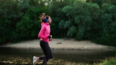 Kulaklık için maraton hazırlanıyor Nehri yakınında bir kız pembe bir ceket ve siyah pantolon çalışır.