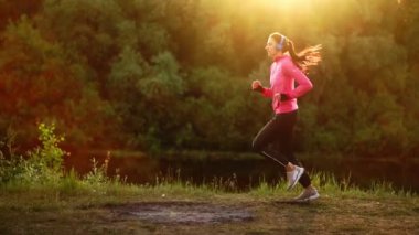 Kulaklığımda uzun saçlı esmer parkta Nehri boyunca gündoğumu pembe bir ceket ve siyah pantolon yaz sabahı çalışır