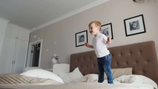 Saltando de la felicidad en la cama mirando burbujas de jabón volando — Vídeos de Stock