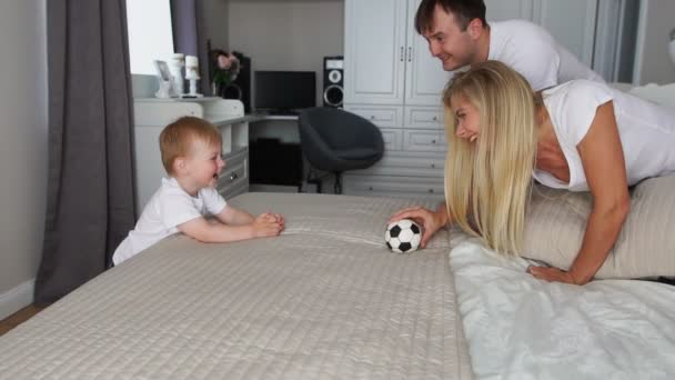 Papa und Mama spielen mit dem Jungen auf dem Bett mit dem Ball — Stockvideo