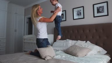 Anne ve oğlu yatakta parlak bir yatak odasında bir çocuk iki yıl gülüyor ve gülümsüyor oynuyorlar