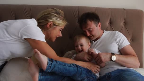 Pais amorosos brincam com seu filho na cama rindo e sorrindo no quarto — Vídeo de Stock