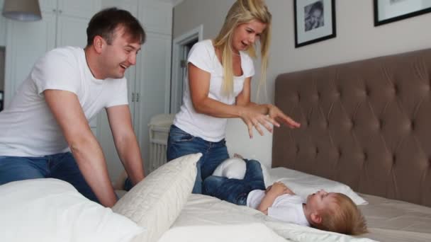 Família feliz jogando a travesseiros luta na cama em casa — Vídeo de Stock