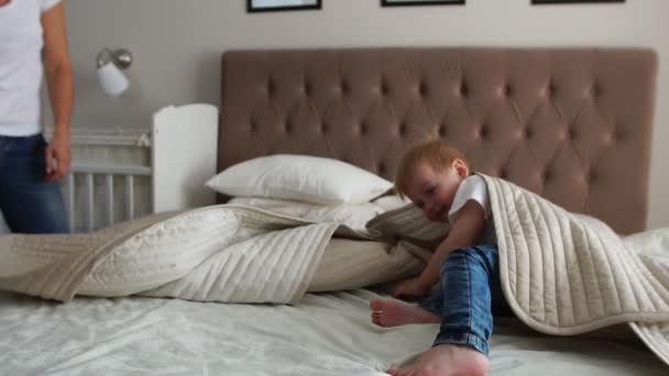 Jovem mãe e pai com seu filho de 2 anos vestido de pijama estão relaxando e brincando na cama no fim de semana juntos, manhã preguiçosa, cena acolhedora e aconchegante. Cores pastel, seletivo — Vídeo de Stock