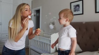 Çocuk ve anne ağır çekimde yatak odasında yatağın üstüne sabun köpüğü ile oynarken