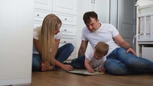 En familj på tre i vita T-shirts och blå jeans sitter på golvet i deras sovrum som leker med pojken i intellektuella spel. Slowmotion-skytte lycklig familj — Stockvideo