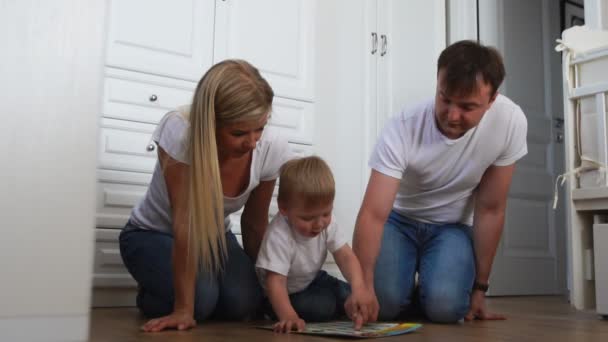 A család három fehér pólók és a kék farmer ült a földön, a hálószobában, a fiú szellemi játékok játszani. Lassú mozgású felvétel boldog család — Stock videók