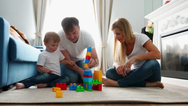 Feliz família pai mãe e bebê 2 anos jogando lego em sua sala de estar brilhante. Atirar em câmera lenta família feliz — Vídeo de Stock